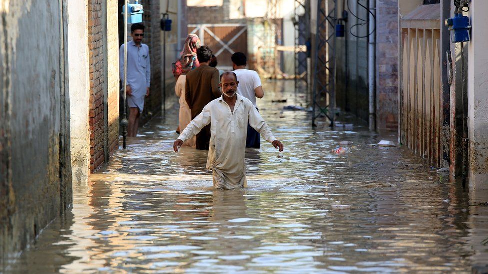 A photo of people walking in a flooded street in Pakistan.