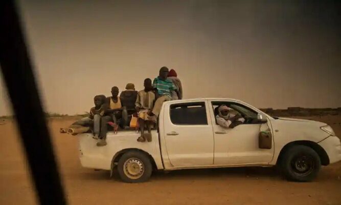 People sit on the open cargo of pick-up trucks, holding wooden sticks tied to the vehicle, as they leave the outskirts of Agadez for Libya. Photograph: Issouf Sanogo/AFP/Getty Images