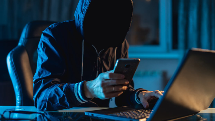 A masked scammer operating a laptop.